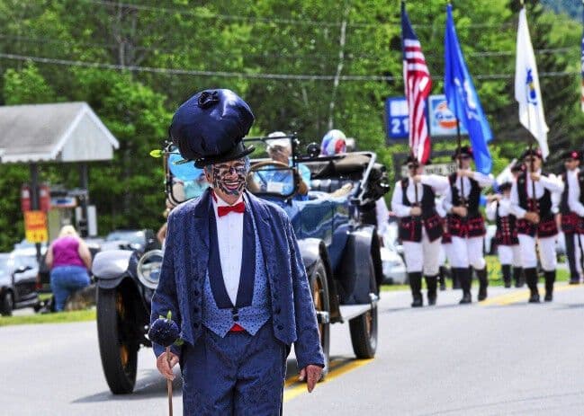 Man dressed as a blueberry costume leading a parade wearing a blueberry hat and suit.