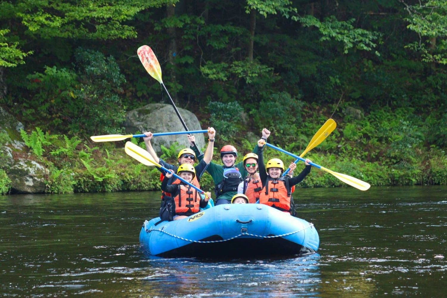 A family in a blue raft holding their yellow paddles up in the air in celebration.